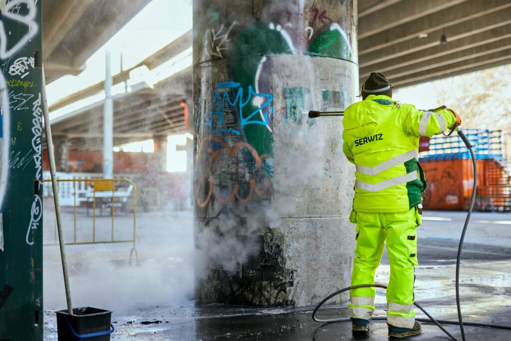 SERWIZ medarbejder fjerner graffiti fra en betonsøjle med højtryksrenser